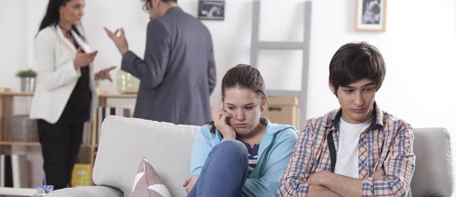 Two young people sitting in silence with worried expressions while adults argue in the background, symbolizing the emotional impact of dealing with addicted friends.