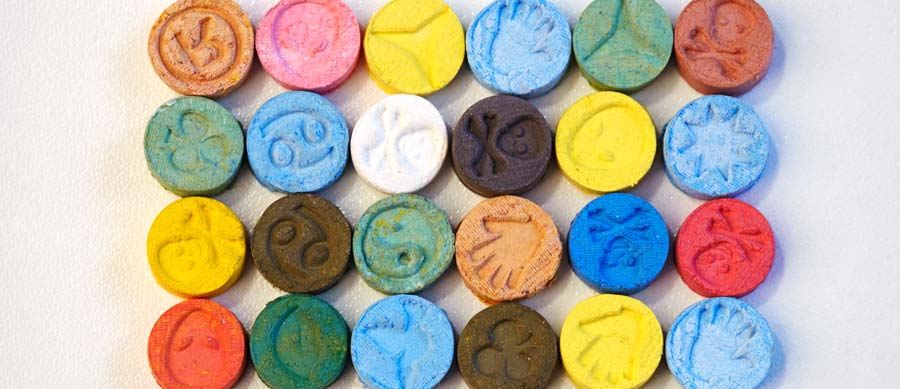 Colorful round tablets embossed with symbols, resembling party pills or ecstasy tablets.