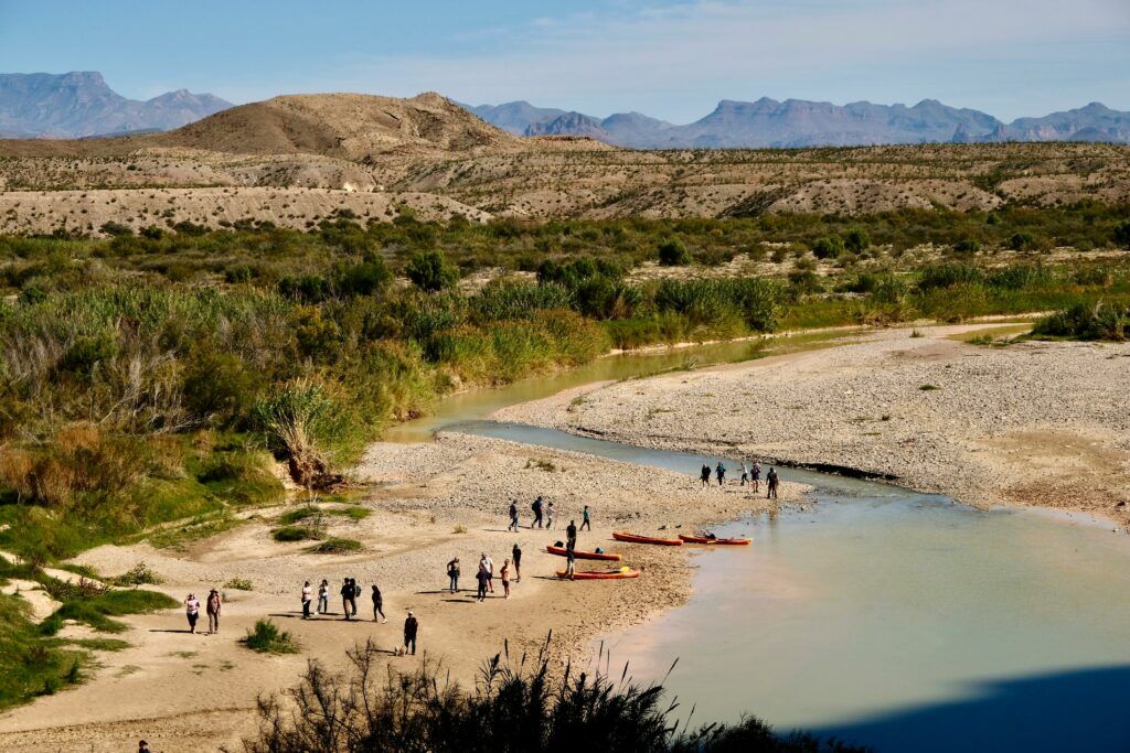 A group of people kayaking and walking along a scenic riverside in a rugged desert landscape, symbolizing the compassionate and guided support offered through professional rehab care.
