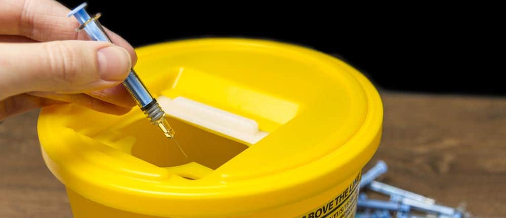Hand disposing of used syringe in a yellow sharps container at a safe injection site.