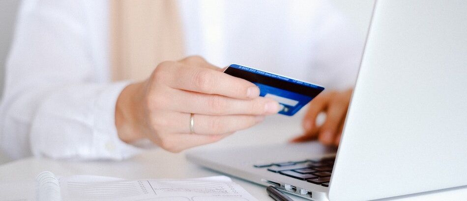 Person holding a credit or bank card near a laptop, symbolizing potential compulsive online shopping or internet-related behavioral addiction
