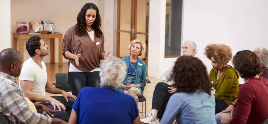 A diverse group of adults in a comfortable circle participating in a guided group therapy session, illustrating personalized and supportive rehabilitation in action.