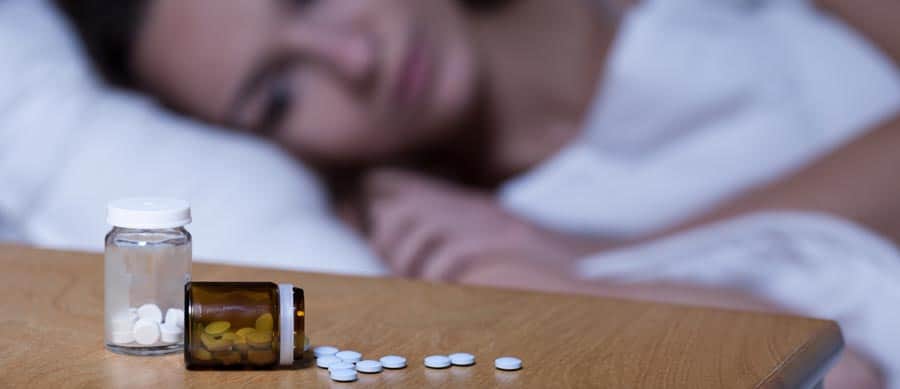 Woman in bed with pill bottles nearby, representing the struggles of dual diagnosis of depression and addiction.
