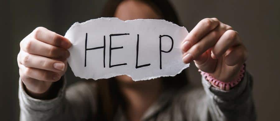 A person holding a paper sign that reads "HELP," conveying a silent plea likely related to substance abuse, domestic violence, or both.