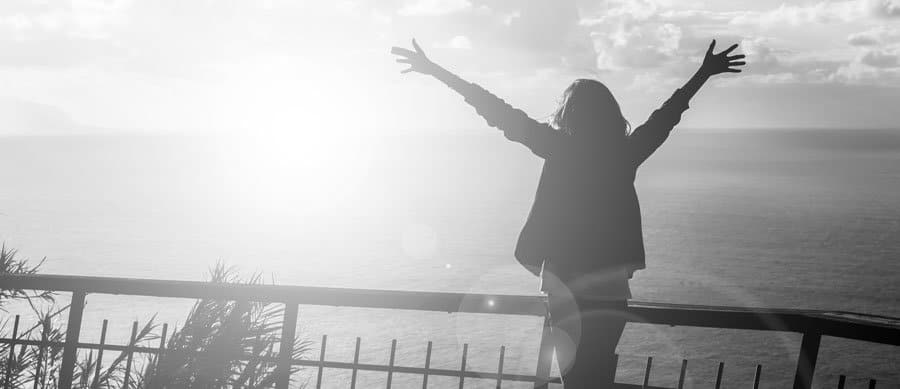Person embracing the sunrise on a balcony, symbolizing spiritual connection, emotional healing, and faith during addiction recovery.