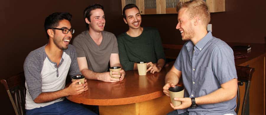 Four young men enjoying a conversation over coffee, showcasing peer support and friendship in addiction recovery.