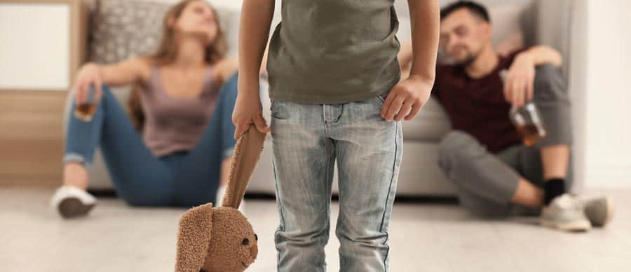 Child holding stuffed animal while parents struggle with alcohol addiction at home.