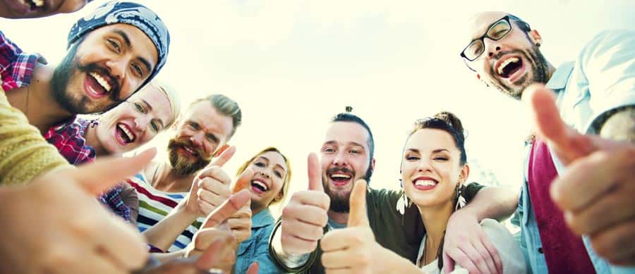 A joyful group of people showing thumbs-up, symbolizing peer support, connection, and positive progress in addiction recovery.