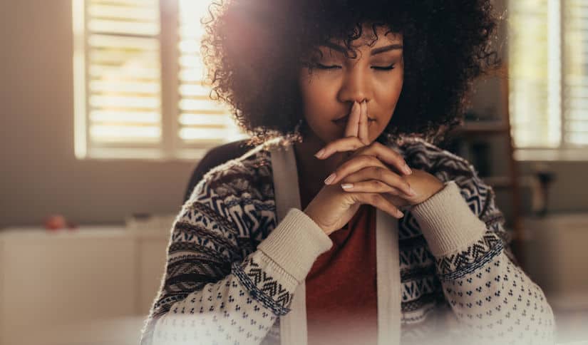 Person with hands clasped under chin, eyes closed, in a reflective moment—suggesting contemplation, inner strength, and the ongoing journey of recovery.