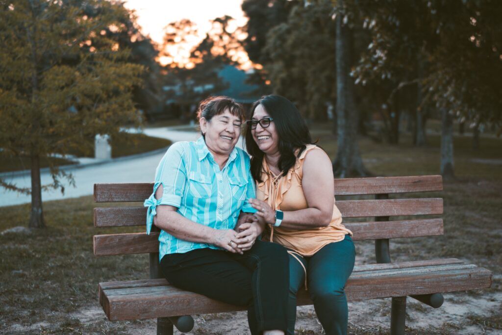 Two women smiling and supporting each other on a park bench, symbolizing recovery and community at a drug rehab center in Austin, Texas.