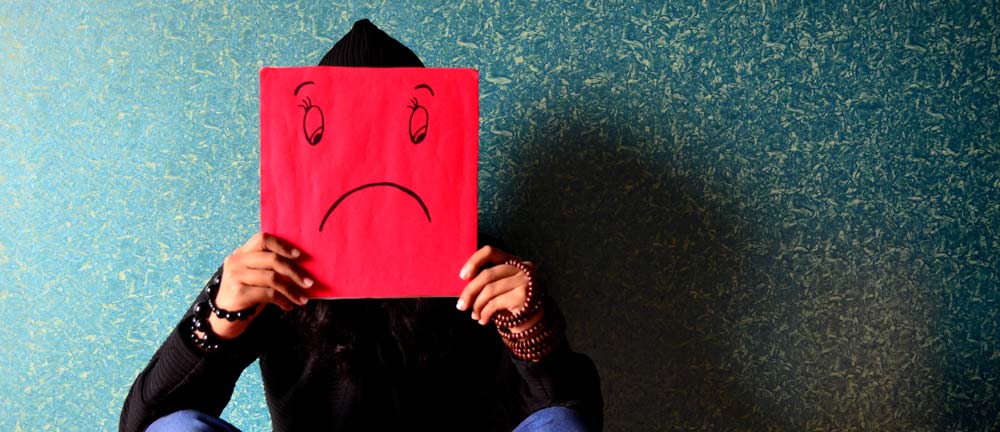 Person hiding face behind sad sign symbolizing grief and substance abuse, reflecting emotional pain and addiction struggles.