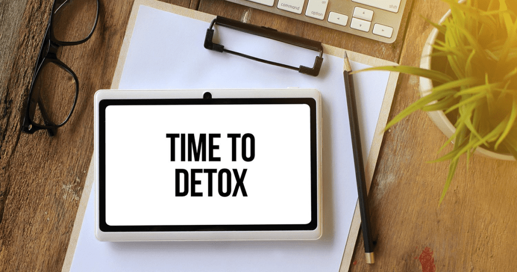 Digital detox for addiction recovery — tablet displaying “Time to Detox” on desk with glasses, pencil, and plant